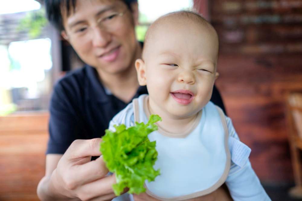 Dad trying to feed greens to baby