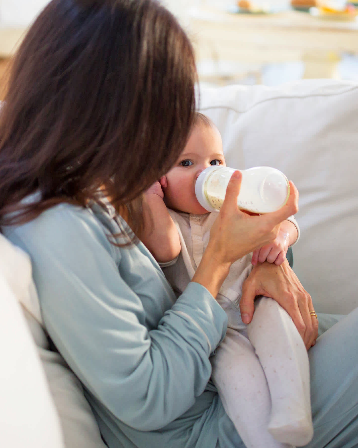 Mom bottle feeding baby on couch