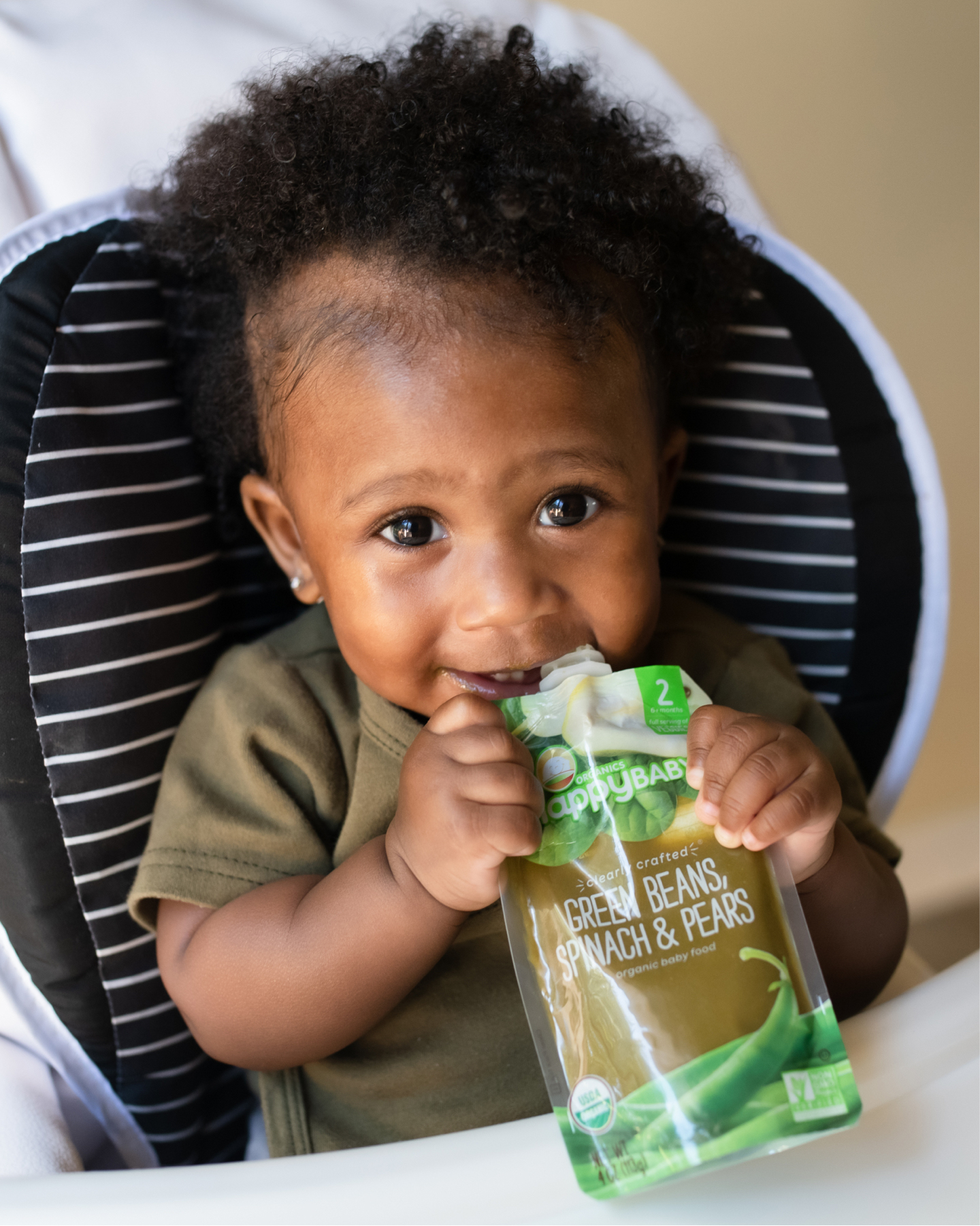 Smiling baby girl eating pouch in a highchair.