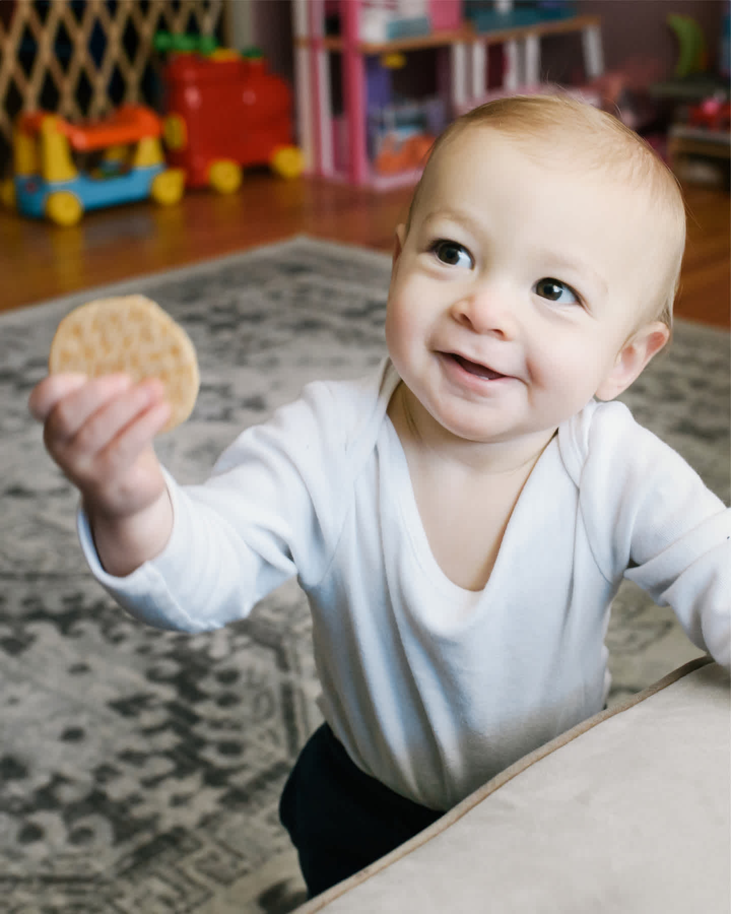 Baby standing and holding up cracker.