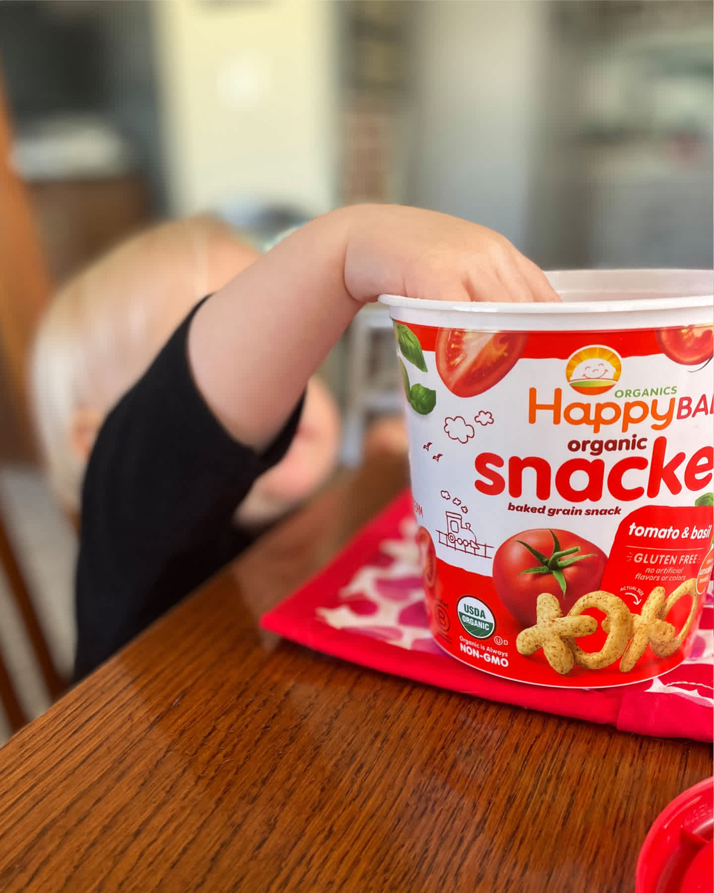 Baby reaching into canister of Happy Baby Snackers on table