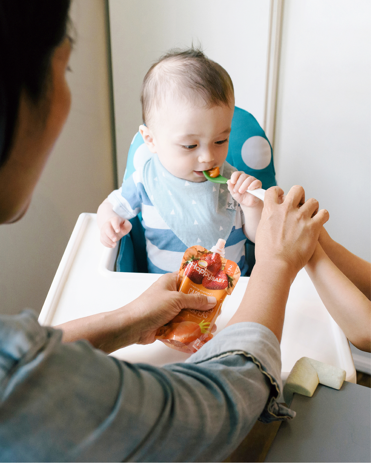 Mom and sister spoon feeding baby brother in highchair.