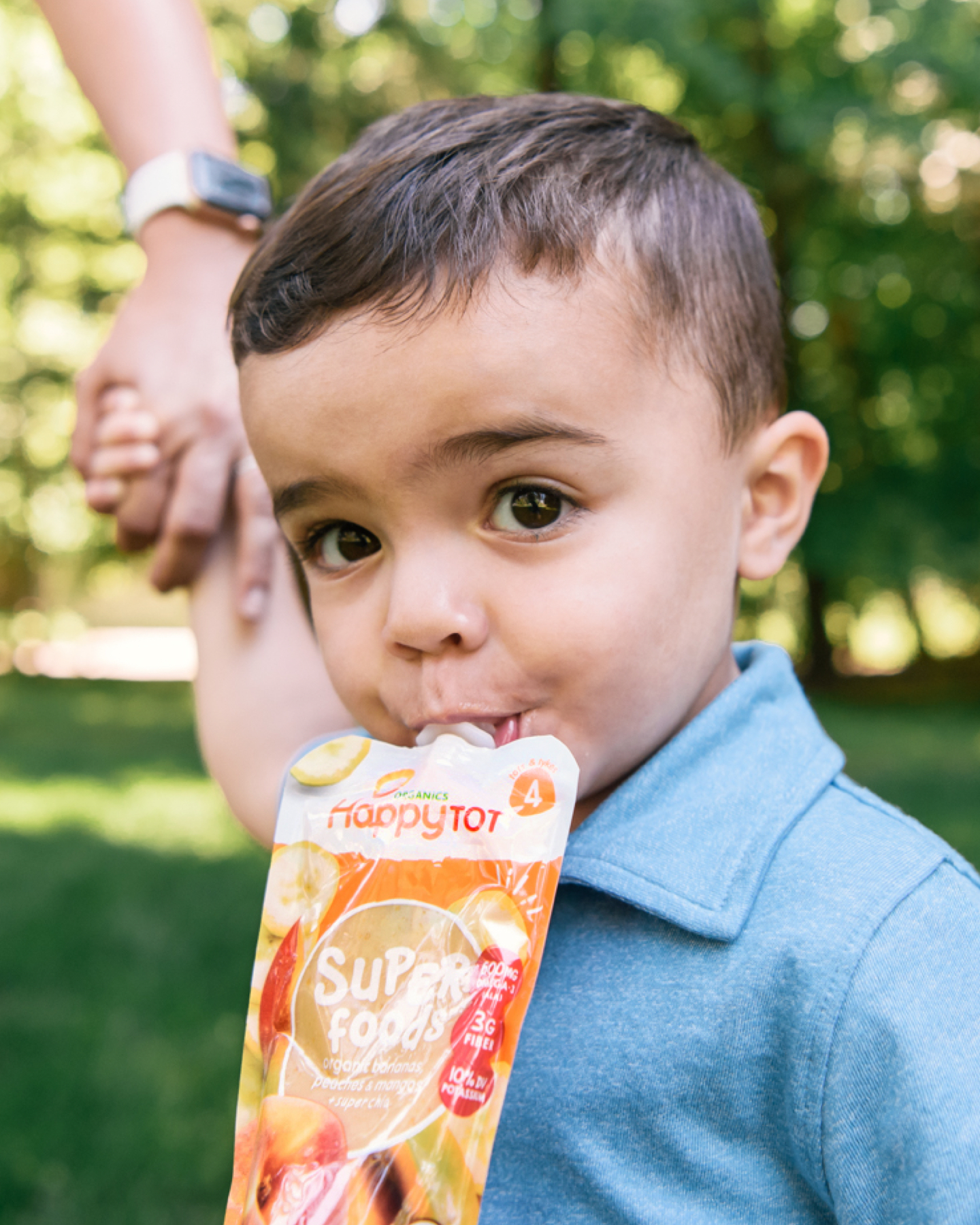 Child eating pouch outside holding his mother's hand