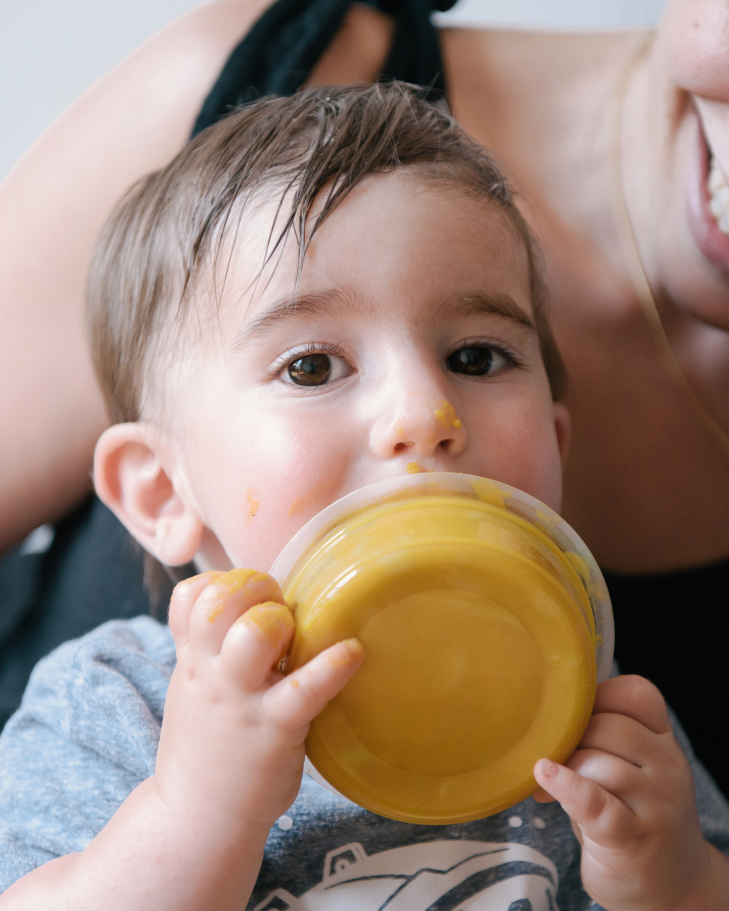 Boy on mother's lap lifting bowl up to his mouth.