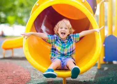 Kind sitzt in Rutsche Lächeln Lachen Spielplatz