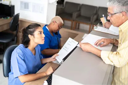 Reception staff assisting a patient with forms at a healthcare front desk.