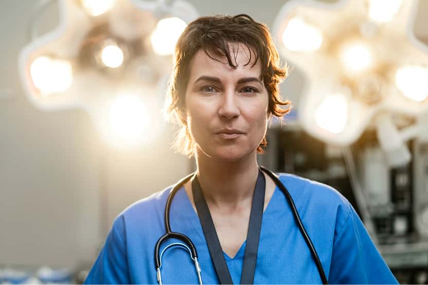 Medical professional in scrubs with a stethoscope under bright surgical lights.