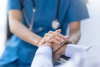 Healthcare professional in blue scrubs holds a patient’s hands in a supportive gesture.
