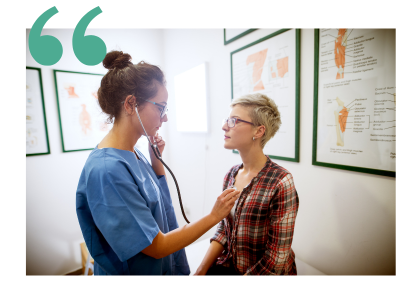 A care provider in blue scrubs is listening to a woman's heart with a stethoscope
