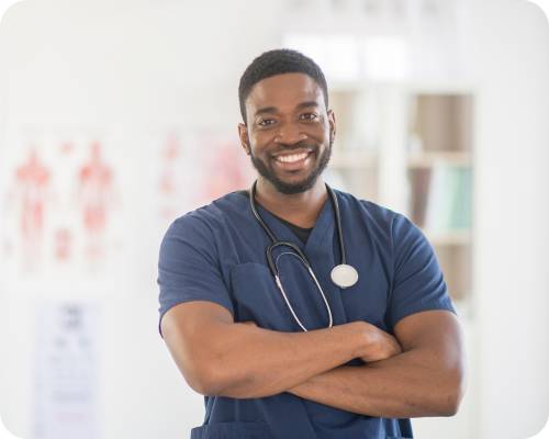 A black nurse practitioner smiles at the camera in a brightly lit facility hallway