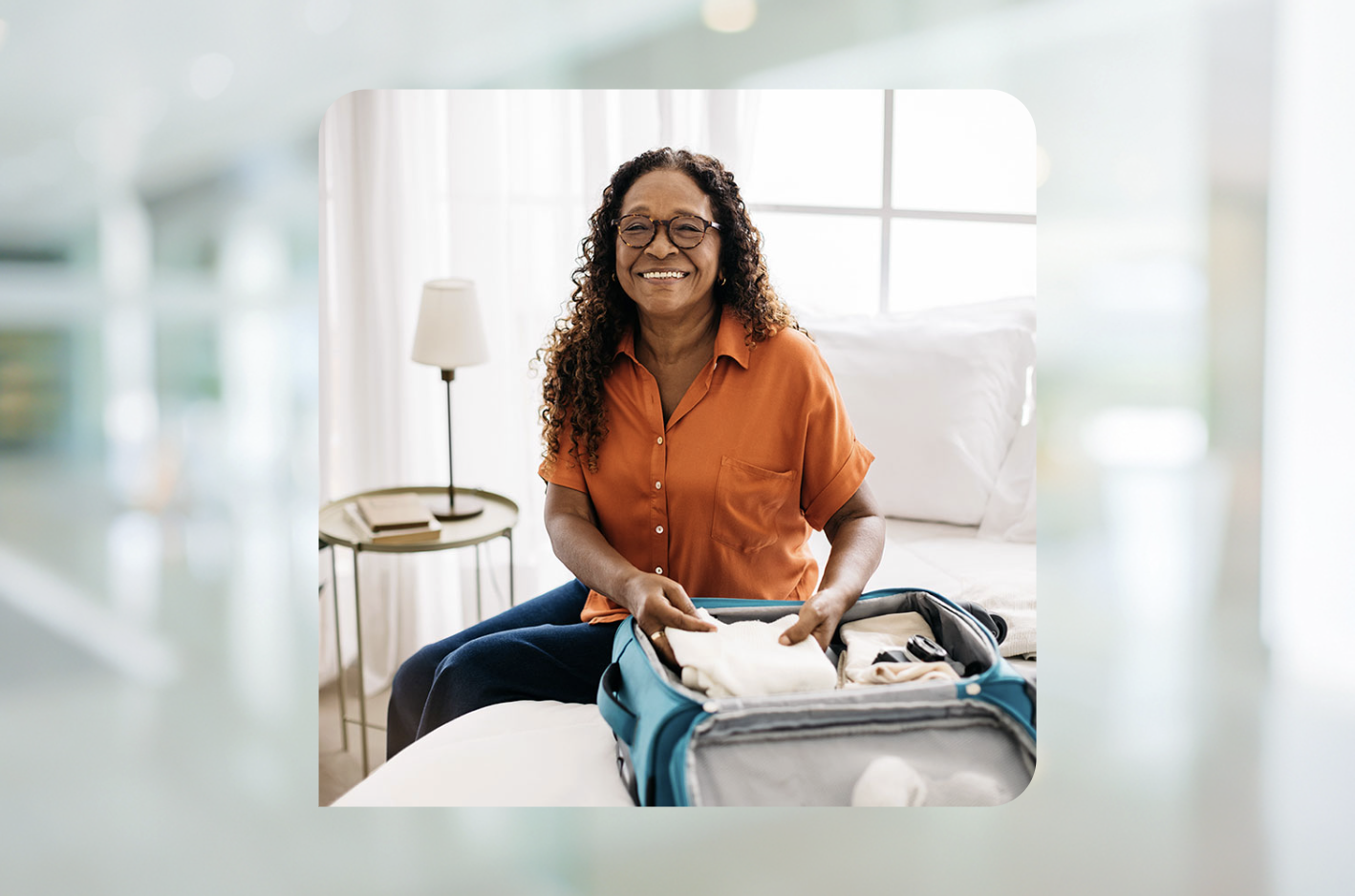 Woman smiles a the camera in a brightly lit room while packing her suitcase