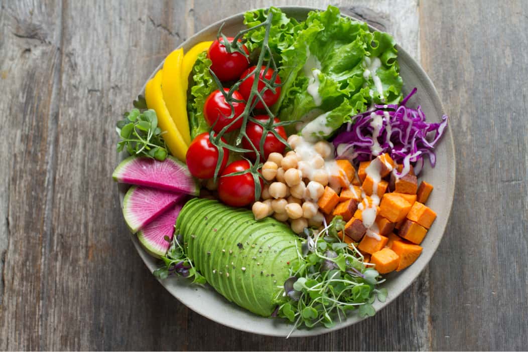 A healthy meal consisting of avocado, tomatoes, sweet potatoes, chickpeas, & more.