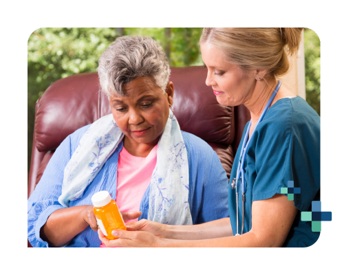 Healthcare professional in scrubs discusses medication with a seated person holding a pill bottle.
