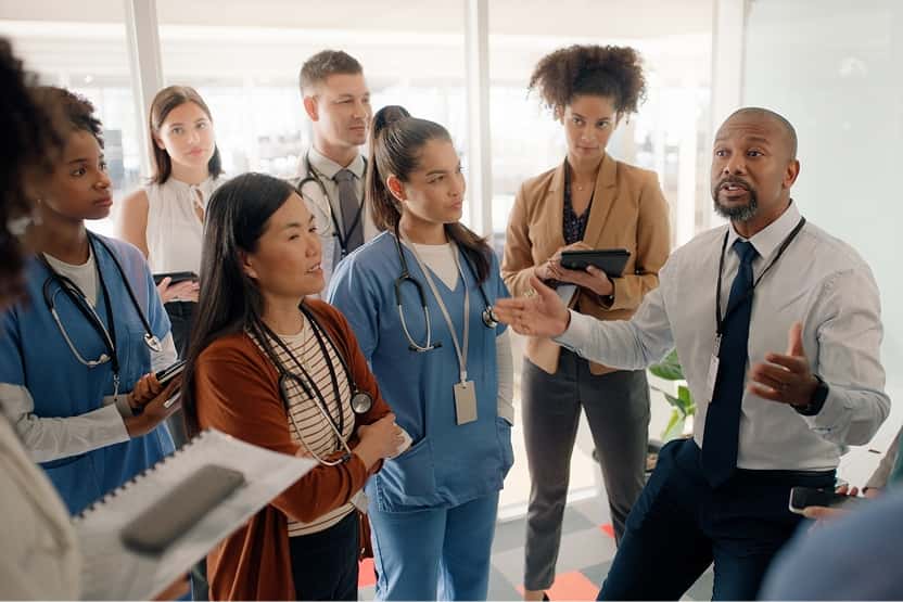 Group of healthcare professionals and staff gathered for a discussion in a bright office setting.