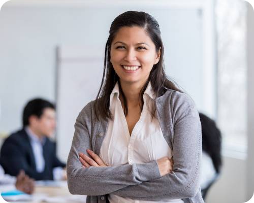 A healthcare administrative assistant smiles with a meeting in the background