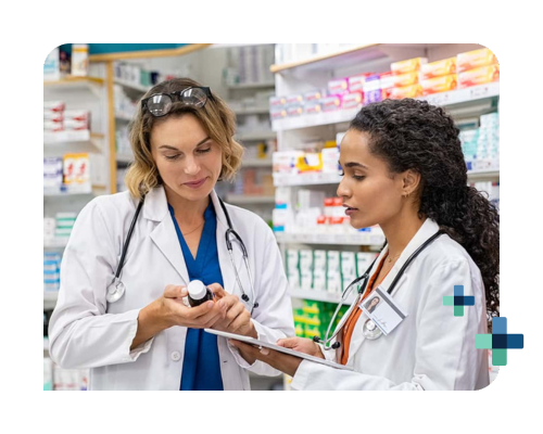 Two pharmacists in lab coats discuss medication while reviewing notes in a pharmacy aisle.