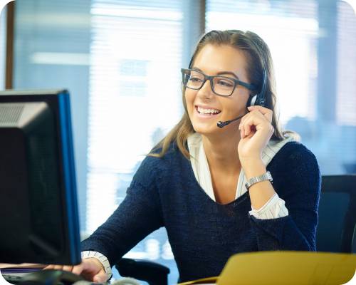 A data entry specialist smiles at her computer while adjusting her headset