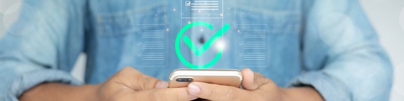 Large green checkmark graphic over an image of a person holding their mobile phone in their hands at a table
