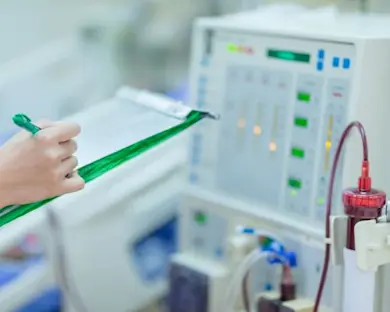 Close up photograph of a dialysis machine with blood flowing and a person using a clipboard nearby