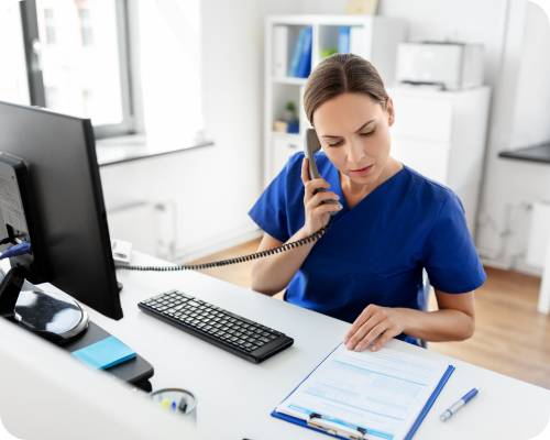 A quality improvement management nurse takes a phone call at her desk while reviewing some paperwork