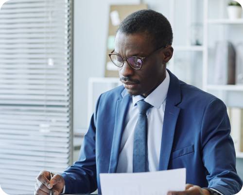 A financial analyst in a suit sits reviewing some paperwork