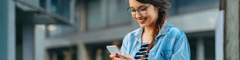 Photograph of a woman in casual attire scrolling on her phone and smiling