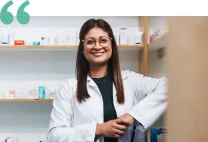 Pharmacist in white coats stand in front of pharmacy shelves.