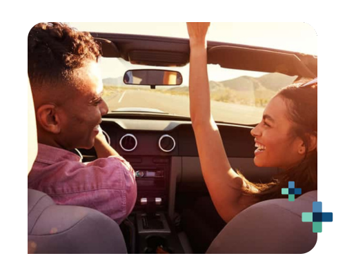 Two people in a convertible on a sunny road trip with mountains in the background.