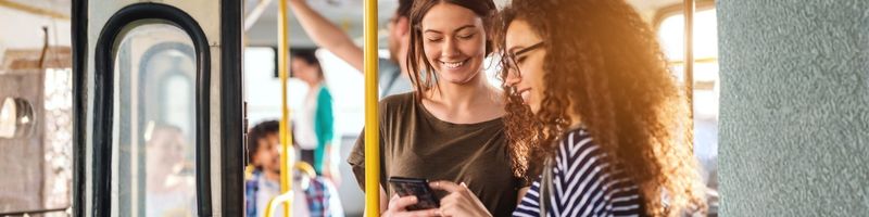 Photograph of two women talking closely on the train, looking together at one of their mobile phones