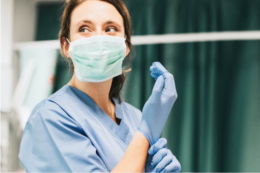 Female nurse with a mask putting on gloves