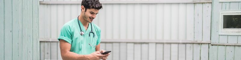 Photograph of a man in scrubs with a stethoscope using his mobile phone