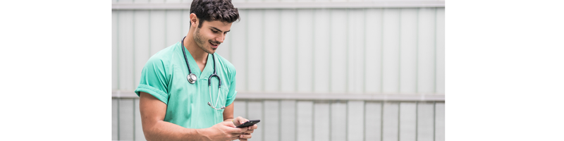 Photograph of a man in scrubs with a stethoscope using his mobile phone