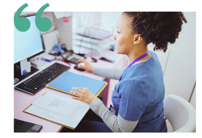 A medical assistant in blue scrubs is looking at documents and using the computer