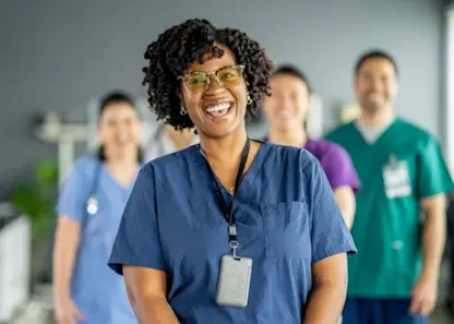 Smiling black nurse in blue scrubs standing in front of coworkers