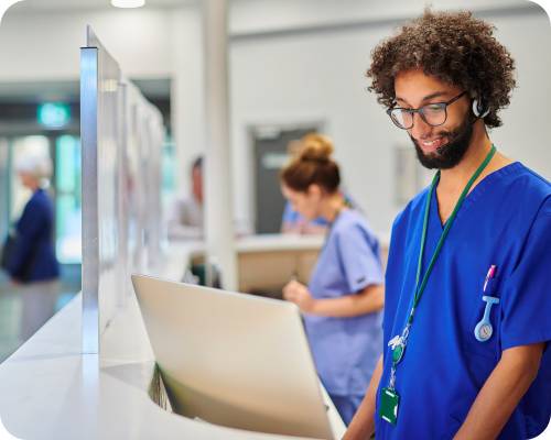 A patient care coordinator smiles while reviewing information on his computer at the station desk