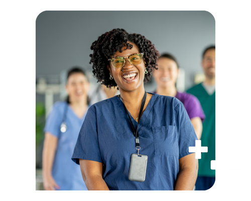 A healthcare professional in navy scrubs laughs in front of the camera; other healthcare professionals wait behind