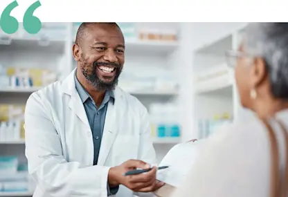 Pharmacist in white coat explains prescription details to a customer in a pharmacy.