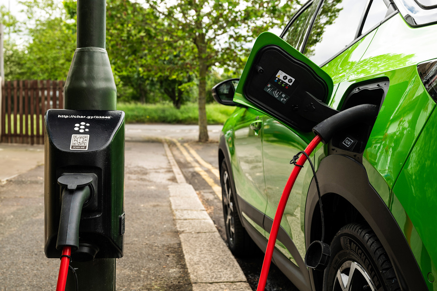 A green electric car connected to a char.gy on-street charge point on a residential street, showing how near-home EV charging can fit around where a car is already parked.