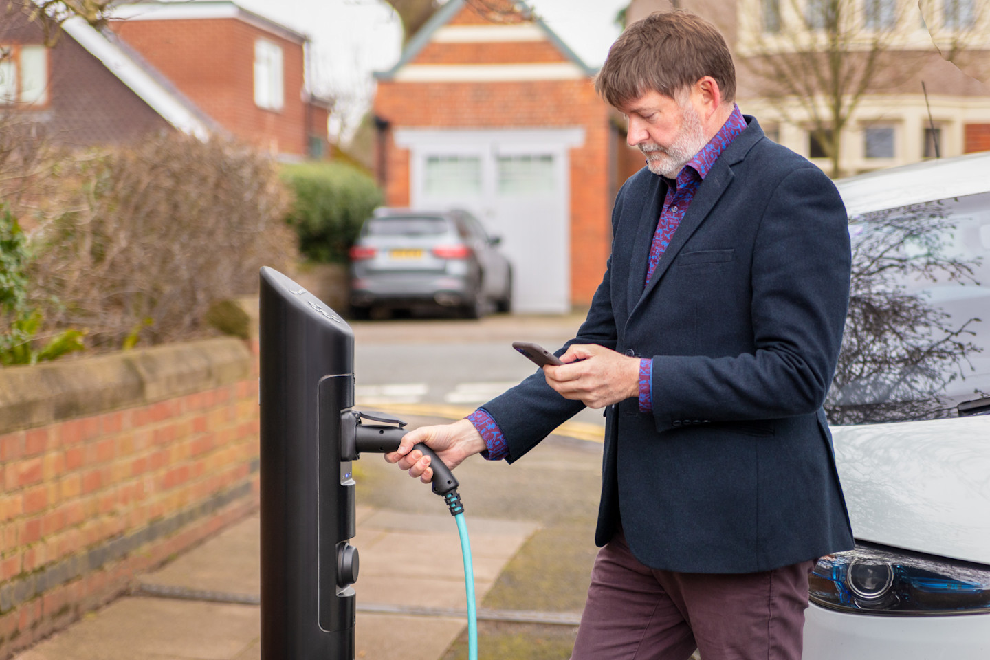 A driver connecting an electric car to a char.gy public charge point, showing the practical process of using an on-street EV charger.