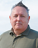 Gary smiles at the camera, wearing a dark green collared shirt against a light background. 