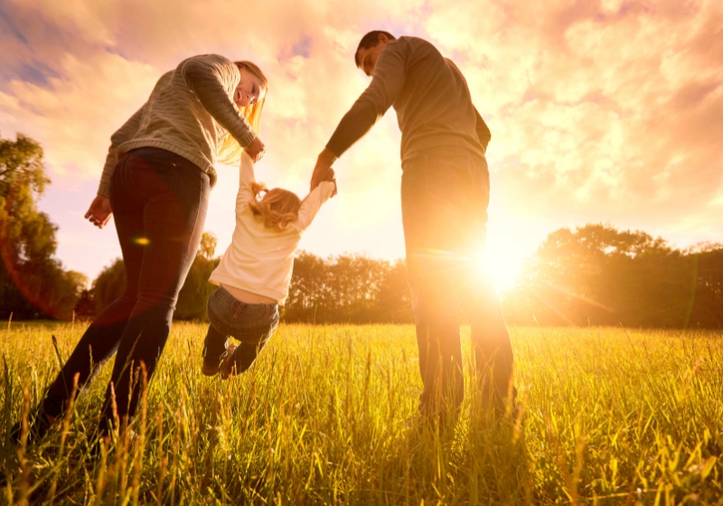 A couple play with their child in a meadow at sunset.