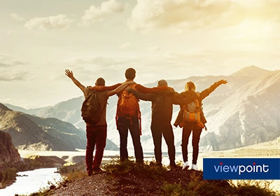 Four people stand with arms outstretched on a mountain.