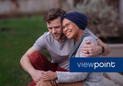 A man embraces a woman who is wearing a head-covering after cancer treatment.