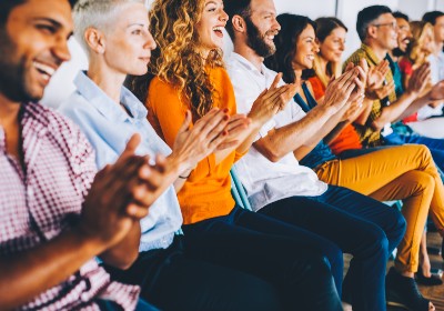 I diverse group of people in the audience is smiling and clapping with excitement