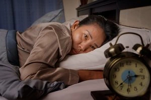 A woman in bed who can't sleep due to insomnia stares tiredly at an alarm clock