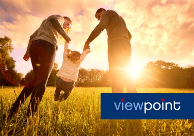 A couple swing their daughter as they walk through grass at sunset. The image banner reads: Viewpoint.