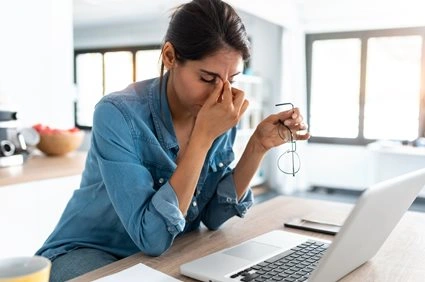 A woman working from home on her laptop pinches her nose with exhaustion.