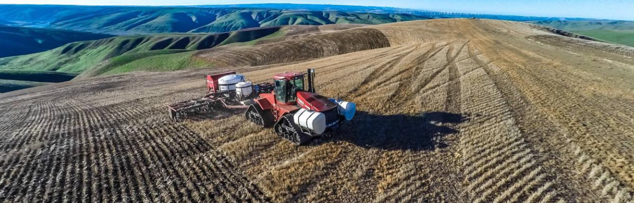 A farmer plants a new crop on a rolling field landscape.