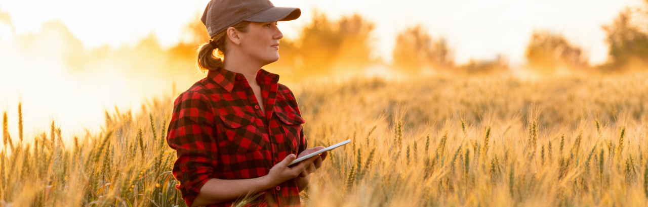A female farmer stands in a field holding a tablet.