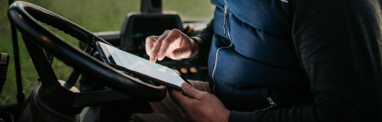 A farmer uses a tablet in the cab of their tractor.